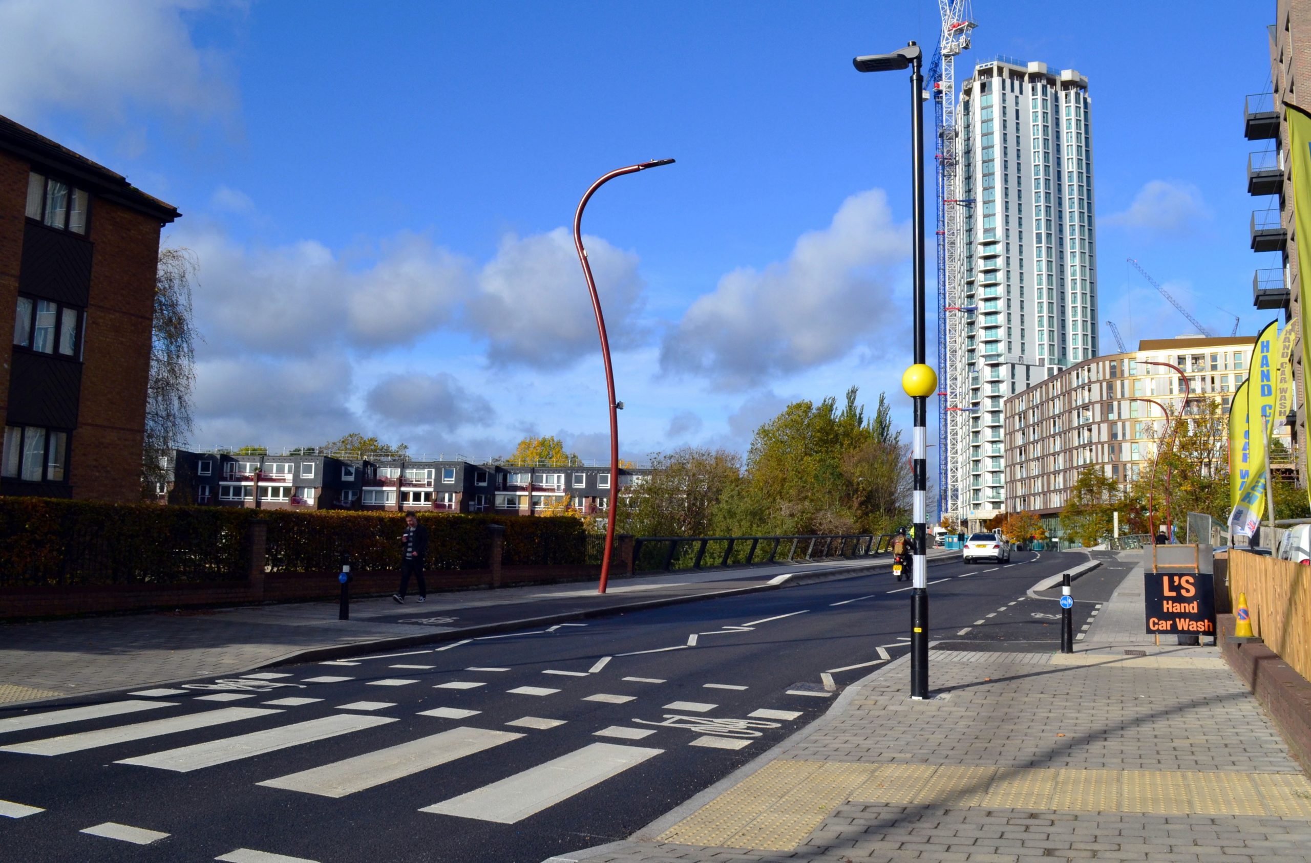 Ferry Lane image showing zebra crossing, street lighting and a building in the background. The sky is mostly blue with some small light grey clouds.